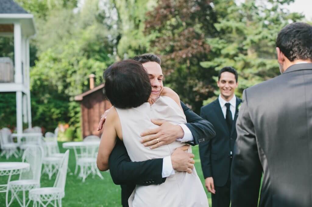 Groom and parent hug at wedding.