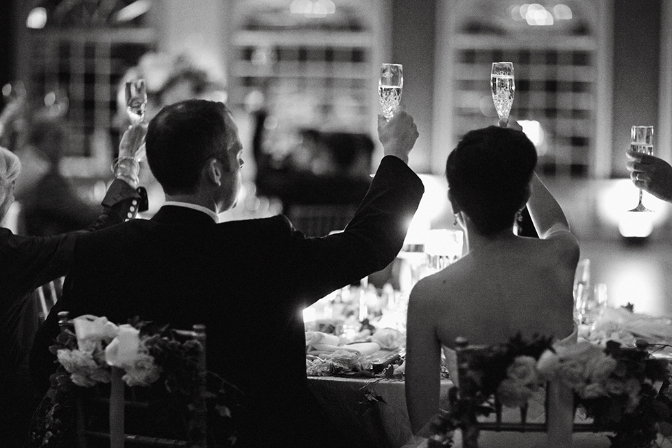 black and white photo of bride and groom raising their glasses during wedding toasts