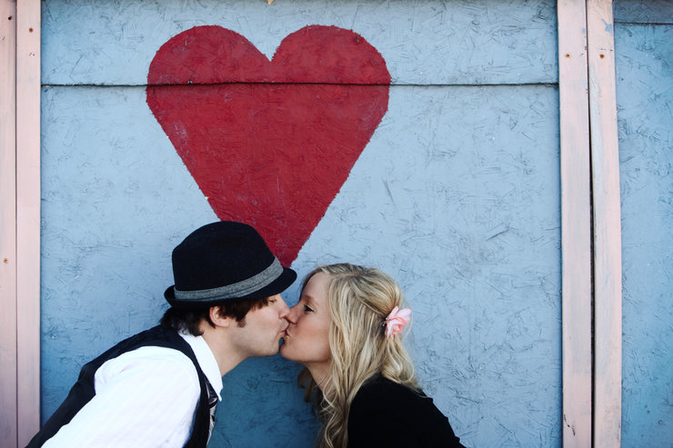 Couple kissing in front of heart wall