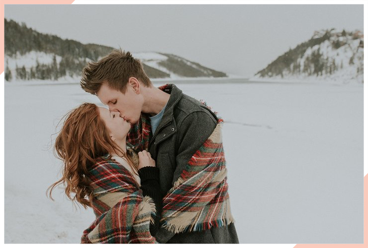 couple kiss on a snow covered field christmas engagement photo