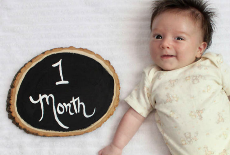 baby smiling with a one month sign
